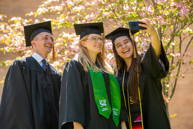 Three graduates taking a selfie in their cap and gowns